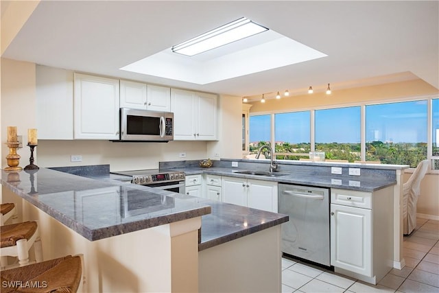 kitchen with stainless steel appliances, white cabinetry, a sink, dark stone counters, and a peninsula