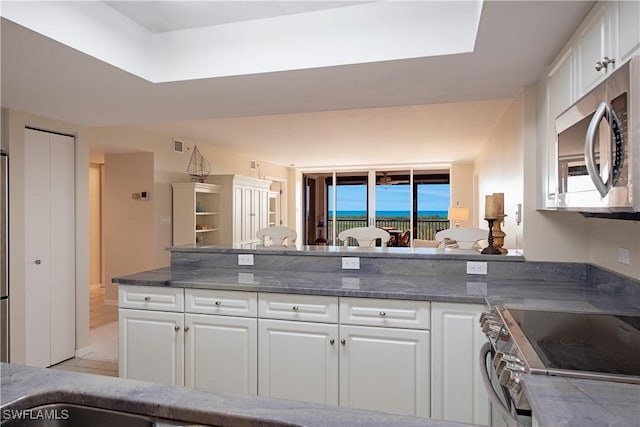 kitchen featuring a peninsula, white cabinetry, appliances with stainless steel finishes, and dark stone countertops