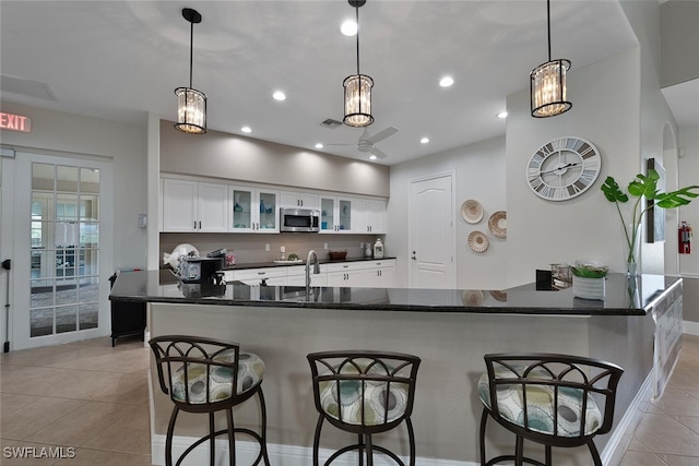 kitchen featuring a breakfast bar, white cabinetry, stainless steel microwave, glass insert cabinets, and pendant lighting