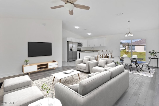 living area with vaulted ceiling, wood finished floors, and ceiling fan with notable chandelier