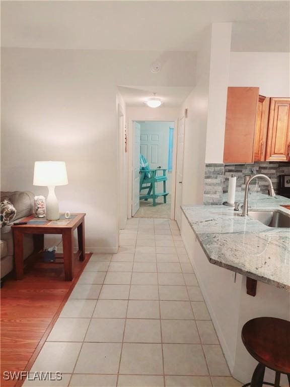 kitchen featuring light tile patterned floors, tasteful backsplash, a breakfast bar, light stone countertops, and a sink