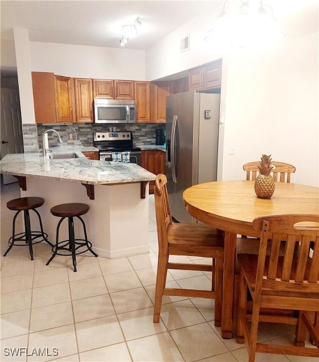 kitchen with light stone counters, stainless steel appliances, a peninsula, a sink, and decorative backsplash