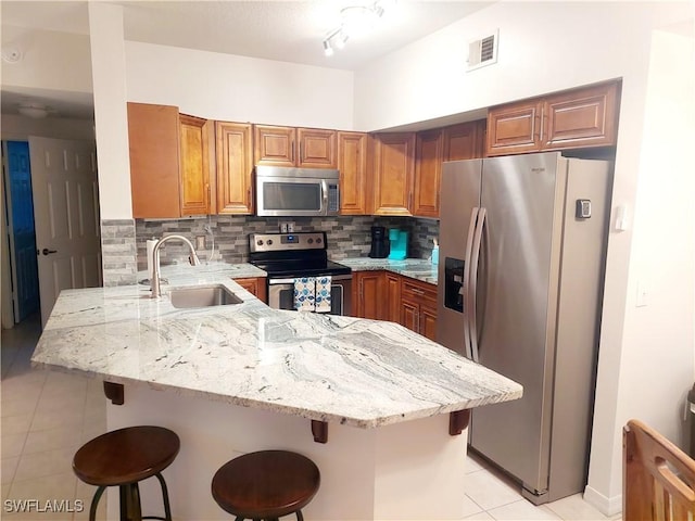 kitchen with light stone counters, a peninsula, a sink, visible vents, and appliances with stainless steel finishes