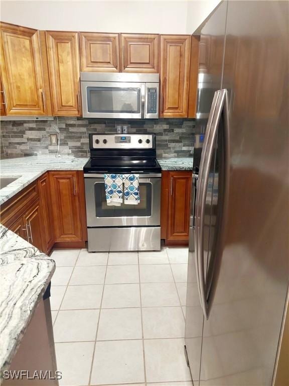 kitchen featuring light tile patterned floors, brown cabinets, light stone countertops, stainless steel appliances, and backsplash