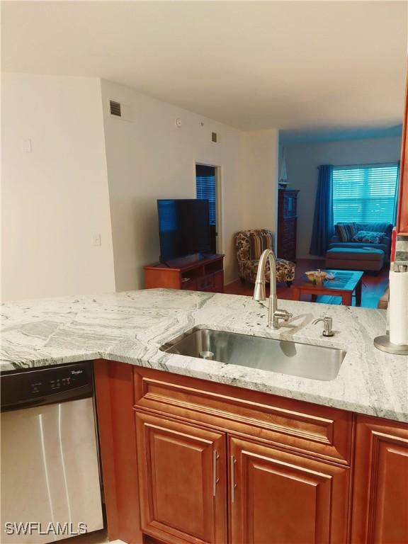 kitchen featuring visible vents, dishwasher, open floor plan, light stone countertops, and a sink