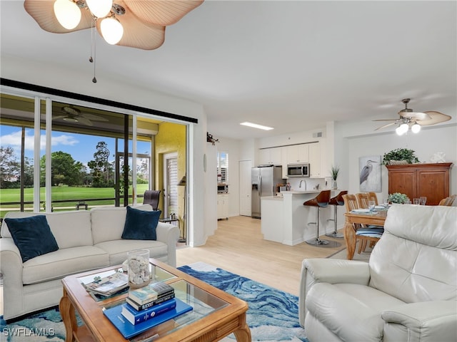 living room featuring a ceiling fan, visible vents, and light wood finished floors