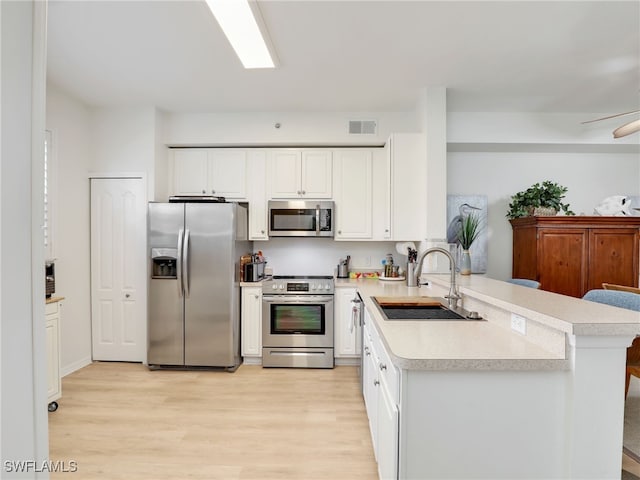 kitchen featuring light wood-type flooring, light countertops, a peninsula, stainless steel appliances, and a sink