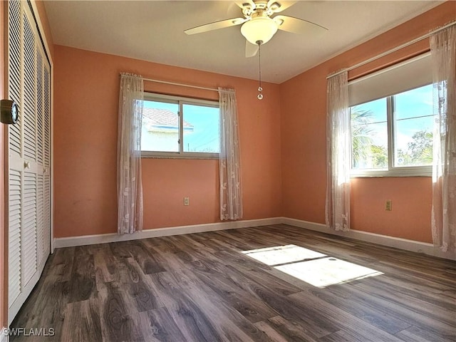 unfurnished bedroom featuring multiple windows, dark wood finished floors, and baseboards