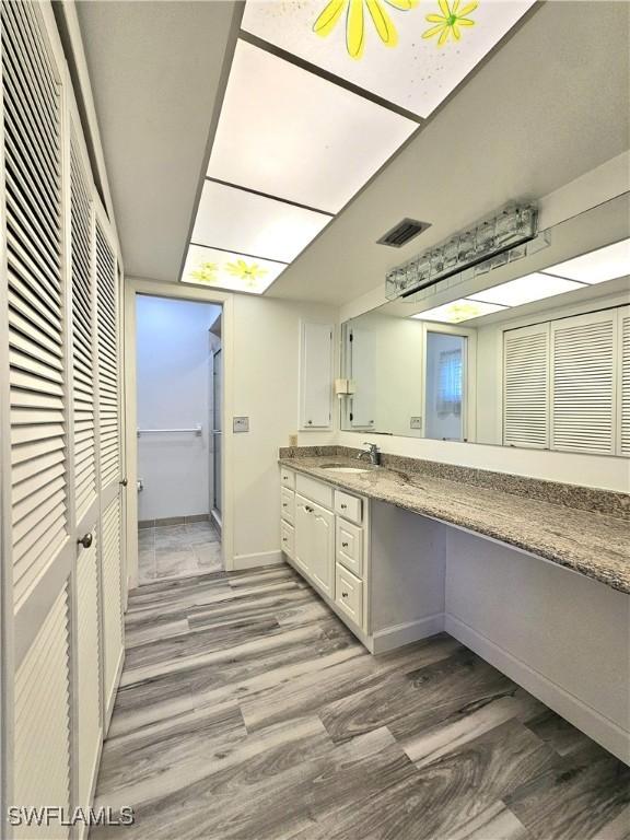 full bathroom with a closet, visible vents, vanity, wood finished floors, and baseboards