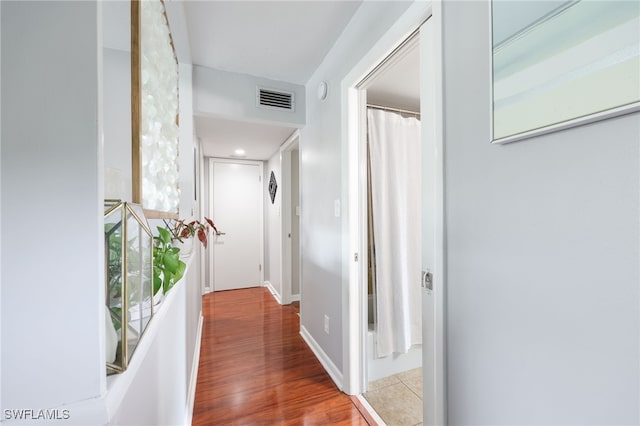 hallway featuring visible vents, baseboards, and wood finished floors