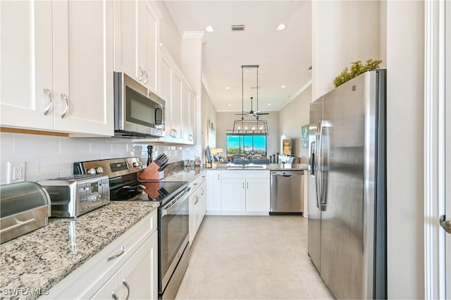 kitchen featuring decorative light fixtures, light stone countertops, stainless steel appliances, white cabinetry, and a sink