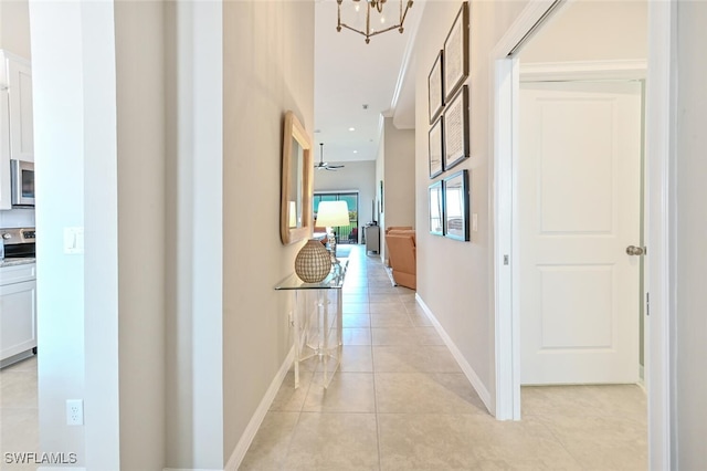 hall featuring light tile patterned floors, baseboards, and a chandelier