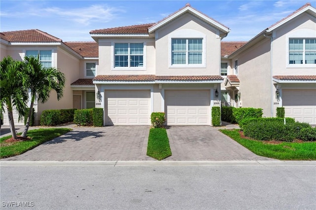 view of front of home with decorative driveway, an attached garage, a tile roof, and stucco siding