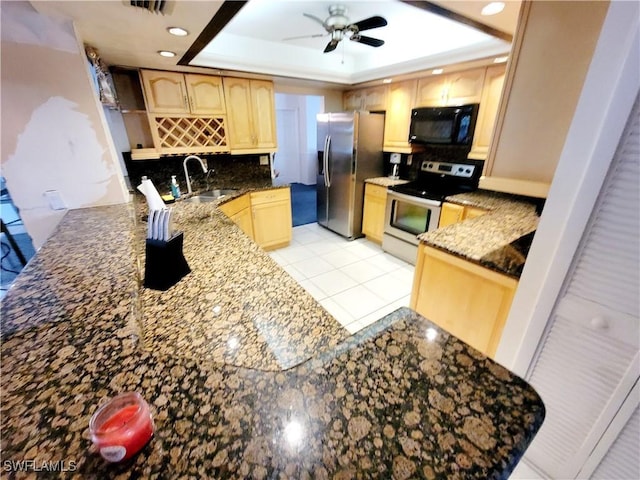 kitchen featuring dark stone counters, stainless steel appliances, a tray ceiling, and light brown cabinets