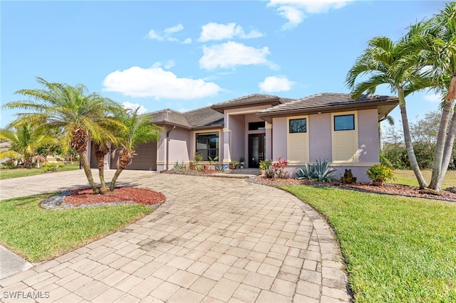 prairie-style house with decorative driveway, stucco siding, a garage, a tiled roof, and a front lawn