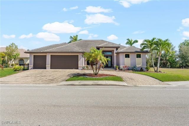 view of front of house featuring a garage, a tiled roof, decorative driveway, stucco siding, and a front lawn