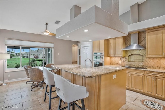 kitchen with stainless steel double oven, black electric cooktop, visible vents, wall chimney exhaust hood, and a center island with sink