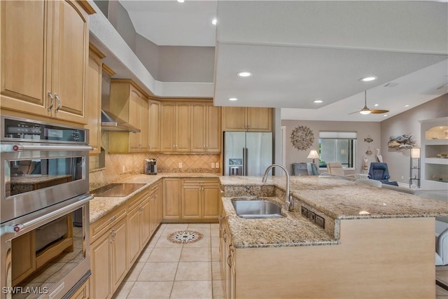 kitchen featuring wall chimney exhaust hood, appliances with stainless steel finishes, light stone countertops, light brown cabinets, and a sink