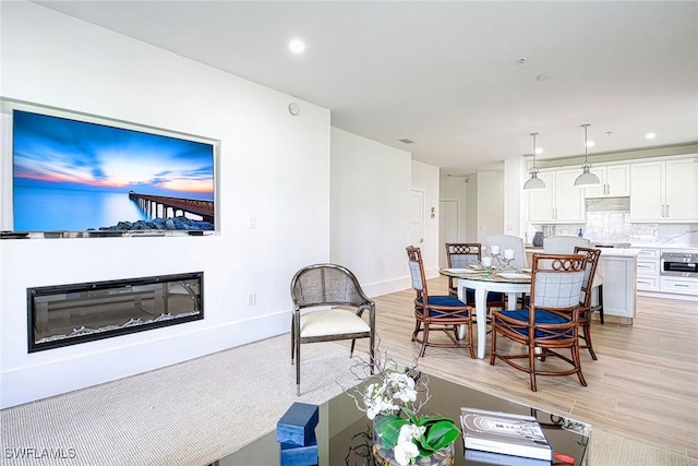 living room with light wood-style floors, recessed lighting, baseboards, and a glass covered fireplace