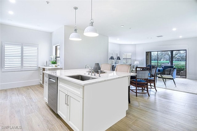 kitchen featuring pendant lighting, open floor plan, white cabinetry, a sink, and an island with sink