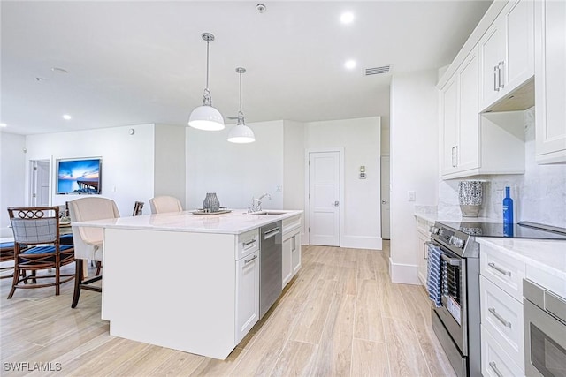 kitchen featuring white cabinets, a breakfast bar area, decorative light fixtures, a kitchen island with sink, and stainless steel appliances