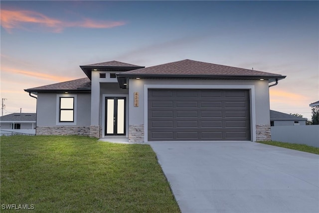 prairie-style house featuring driveway, stone siding, stucco siding, and a yard