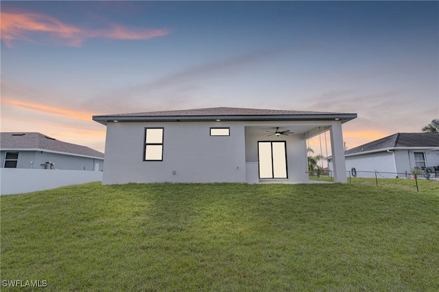 back of property featuring a ceiling fan, a yard, fence, and stucco siding