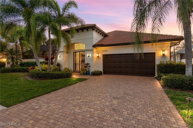 mediterranean / spanish home with stucco siding, a tile roof, an attached garage, decorative driveway, and a front yard