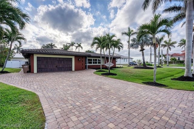 view of front facade featuring a garage, a tiled roof, decorative driveway, a front lawn, and stucco siding