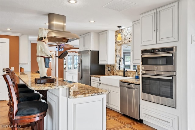 kitchen featuring appliances with stainless steel finishes, white cabinetry, island exhaust hood, and a sink