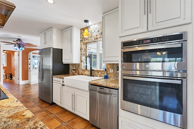 kitchen featuring tasteful backsplash, arched walkways, white cabinets, appliances with stainless steel finishes, and a sink