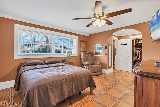 bedroom with baseboards, a spacious closet, ornamental molding, and arched walkways