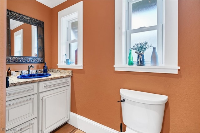 half bathroom with toilet, vanity, and baseboards