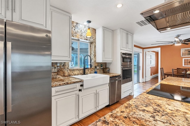 kitchen with a sink, a ceiling fan, white cabinets, appliances with stainless steel finishes, and range hood