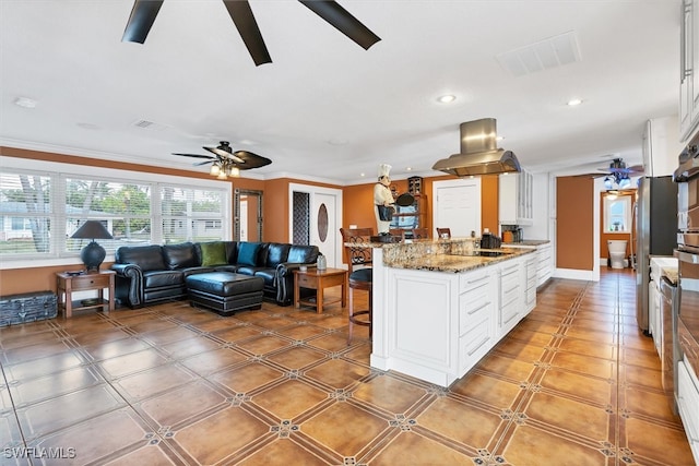 kitchen featuring ceiling fan, island exhaust hood, visible vents, and white cabinets