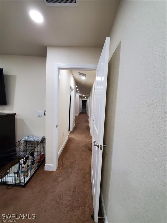 corridor featuring visible vents, baseboards, and dark colored carpet