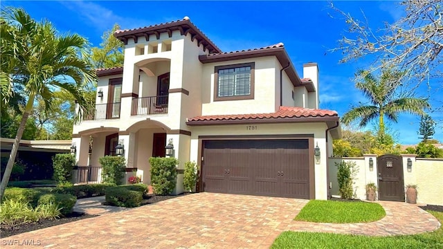 mediterranean / spanish-style home with a balcony, a chimney, an attached garage, decorative driveway, and stucco siding