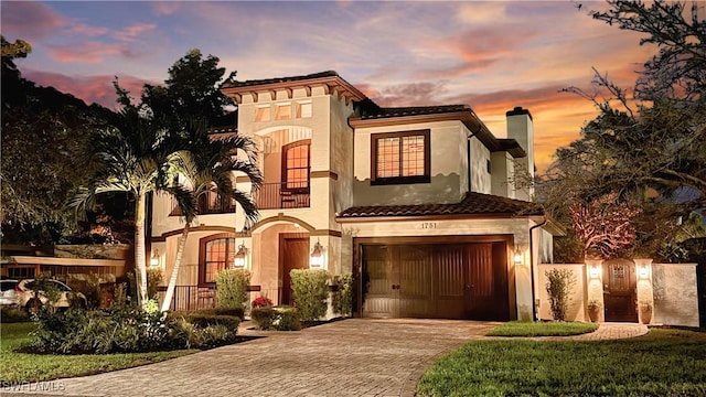 mediterranean / spanish house featuring an attached garage, a tile roof, decorative driveway, stucco siding, and a chimney