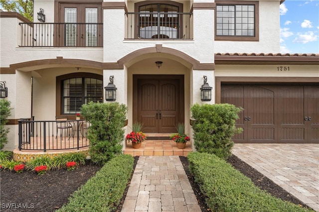 doorway to property with a balcony, driveway, an attached garage, and stucco siding