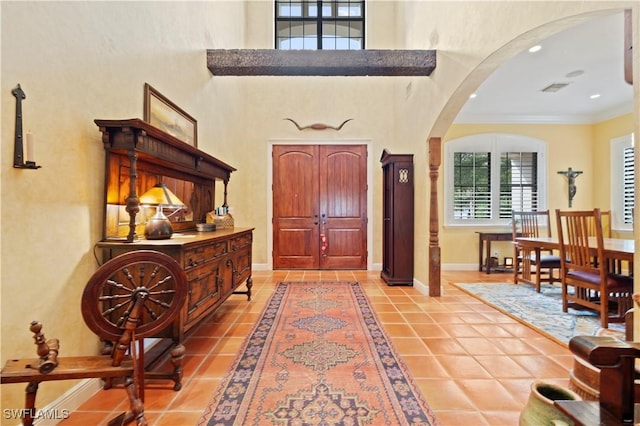 foyer entrance with arched walkways, a towering ceiling, ornamental molding, light tile patterned flooring, and baseboards