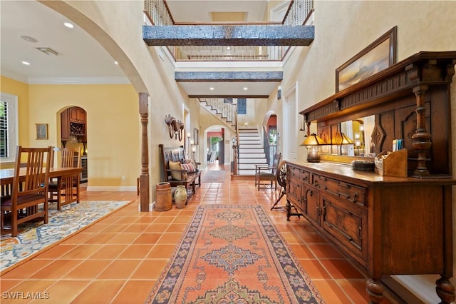 tiled foyer featuring arched walkways, a healthy amount of sunlight, crown molding, and a high ceiling