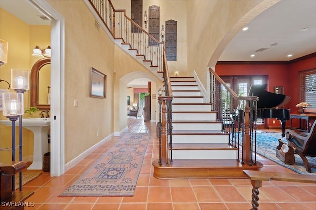 tiled entryway featuring a towering ceiling, baseboards, stairs, and arched walkways