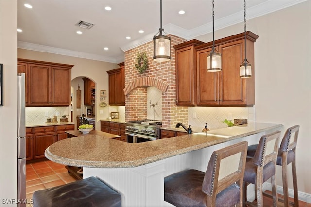 kitchen featuring visible vents, hanging light fixtures, appliances with stainless steel finishes, brown cabinetry, and a kitchen bar