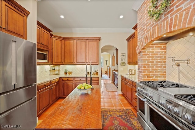 kitchen with arched walkways, ornamental molding, high end appliances, and backsplash