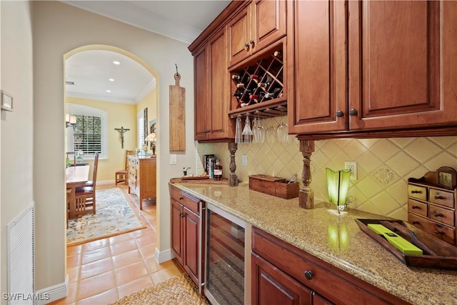 kitchen with beverage cooler, visible vents, arched walkways, light stone counters, and crown molding