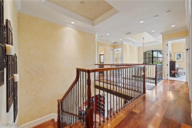 corridor featuring baseboards, wood finished floors, a tray ceiling, crown molding, and an upstairs landing