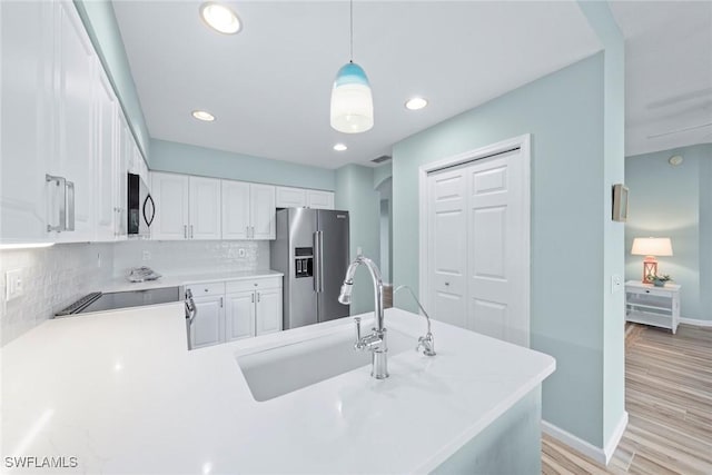 kitchen with light countertops, decorative backsplash, appliances with stainless steel finishes, white cabinetry, and a sink