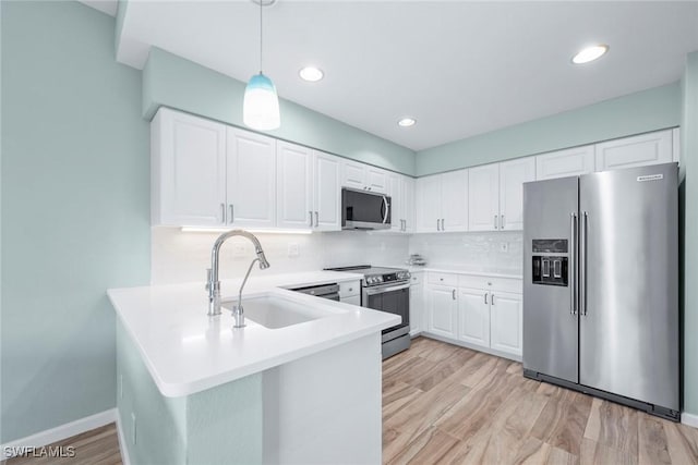 kitchen with stainless steel appliances, a peninsula, a sink, white cabinets, and tasteful backsplash