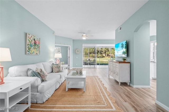 living area featuring arched walkways, light wood finished floors, visible vents, ceiling fan, and baseboards