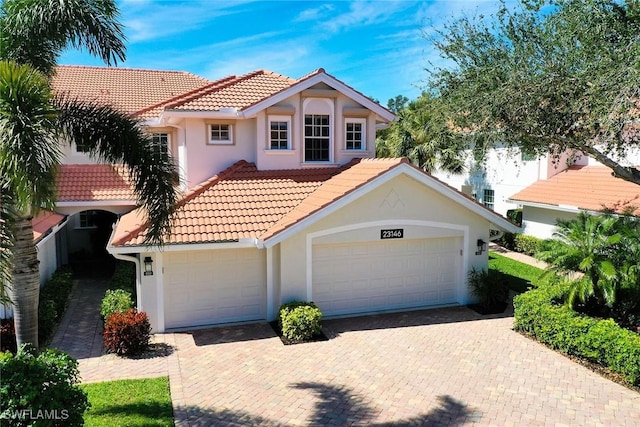 mediterranean / spanish home featuring a garage, a tiled roof, decorative driveway, and stucco siding